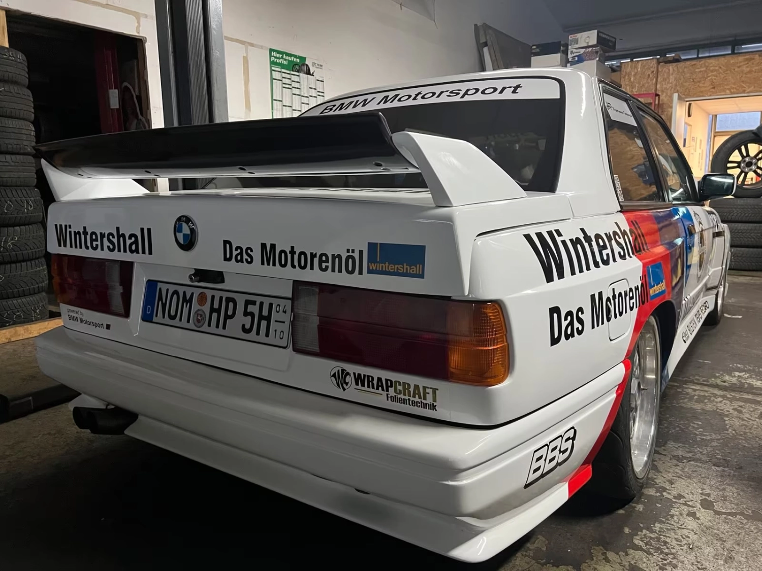 Heck des weißen BMW E30 M3 DTM mit Wintershall-Motorsport-Beklebung in der Werkstatt