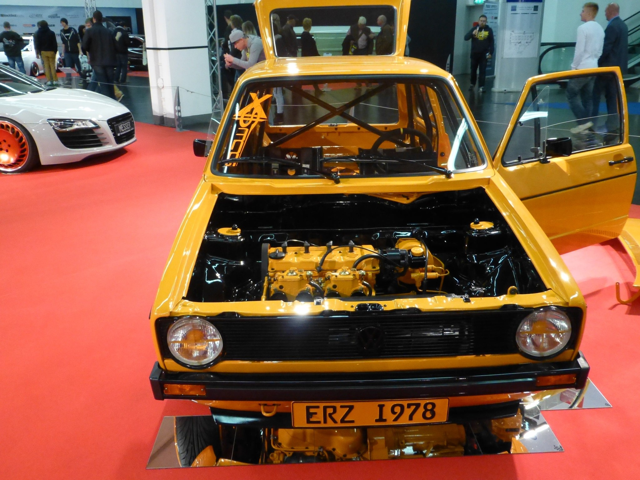 Getunter gelber VW Golf mit geöffneter Motorhaube und Überrollkäfig auf einer Ausstellung